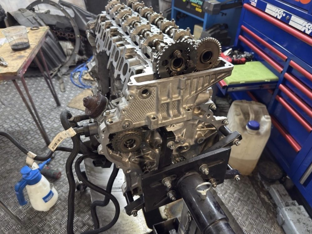 A BMW engine stripped down on the bench, cylinder head and timing gears exposed