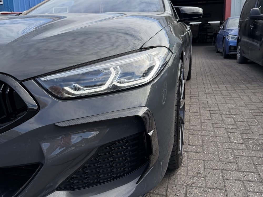 A grey BMW M8 with carbon fibre front splitter and canards fitted, outside the workshop