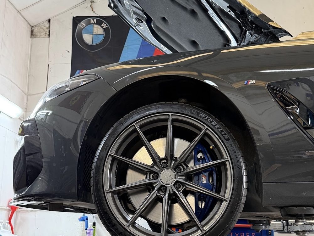 A BMW M8 raised on the ramp, showing the wheel and blue M brake calipers