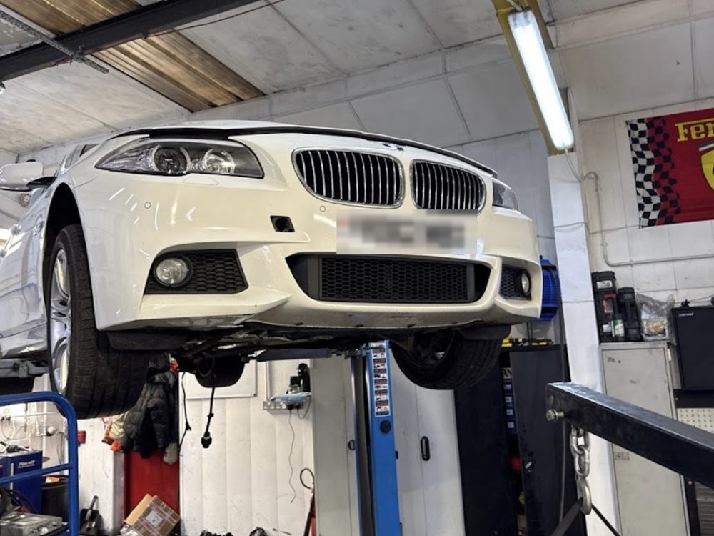 A white BMW 5 Series raised on the two-post ramp inside the workshop