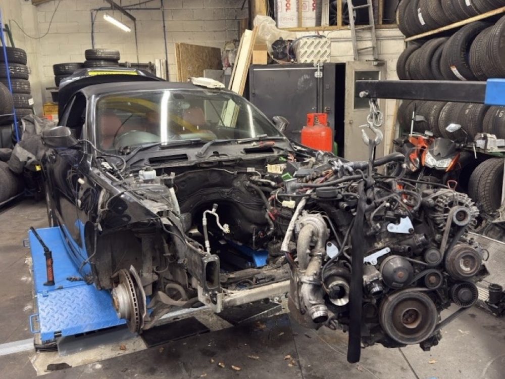 A stripped BMW with its engine and turbocharger removed and sitting alongside